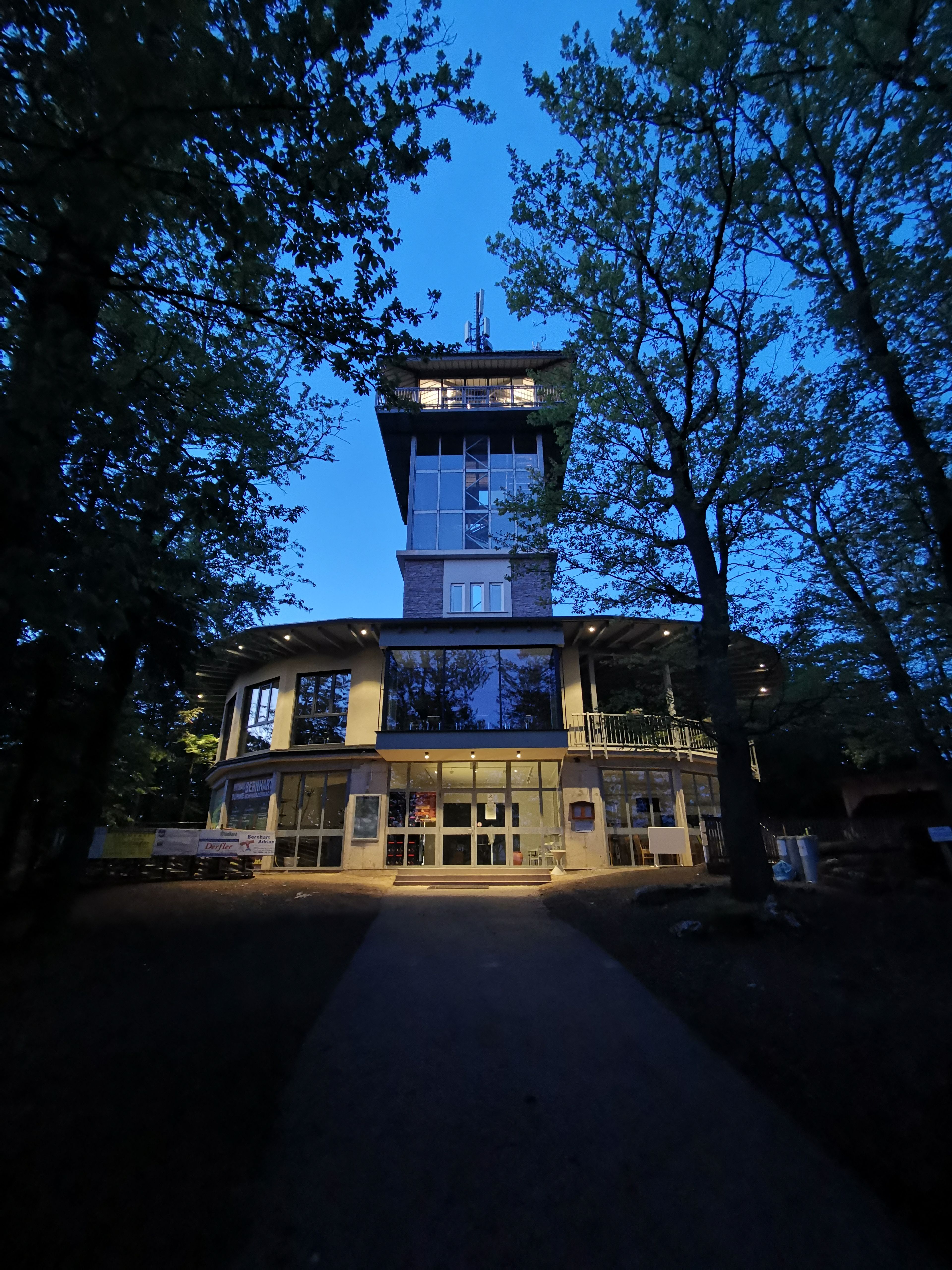 Oválná budova s prosklenou vyhlídkovou věží v noci.