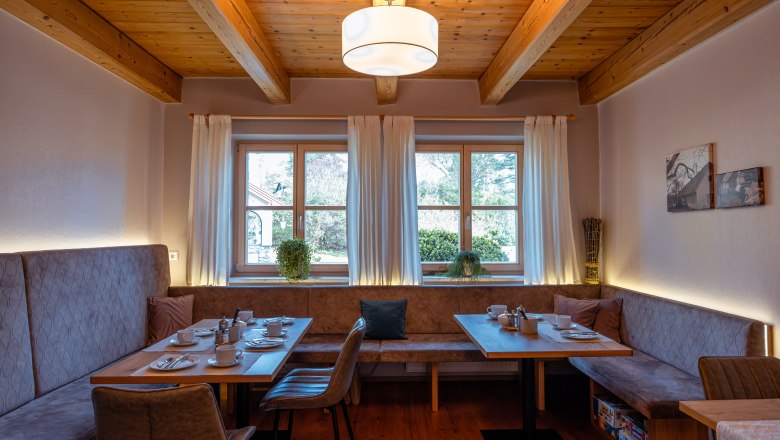 &Uacute;tuln&aacute; j&iacute;delna s dřevěn&yacute;m tr&aacute;mov&yacute;m stropem, oknem a prostřen&yacute;m stolem.