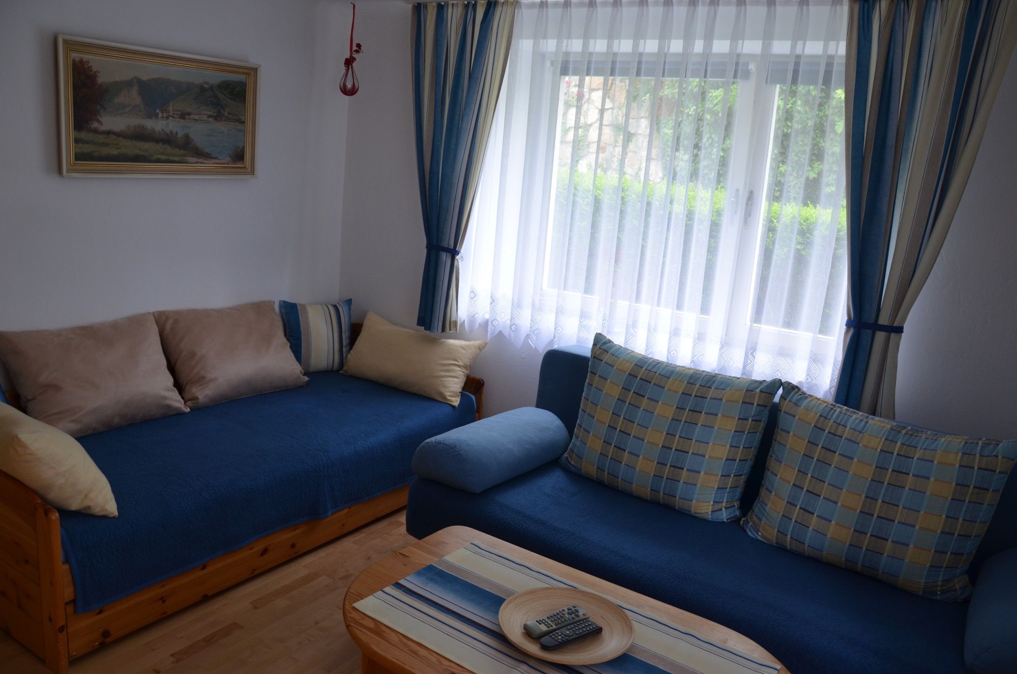 Útulný obývací pokoj s modrou pohovkou, polštáři, dřevěným stolem a oknem se závěsy.