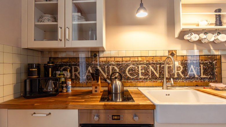 Kuchyňská linka s dřevěnou linkou, dřezem, varnou deskou a mozaikovou dlažbou s "GRAND CENTRAL".