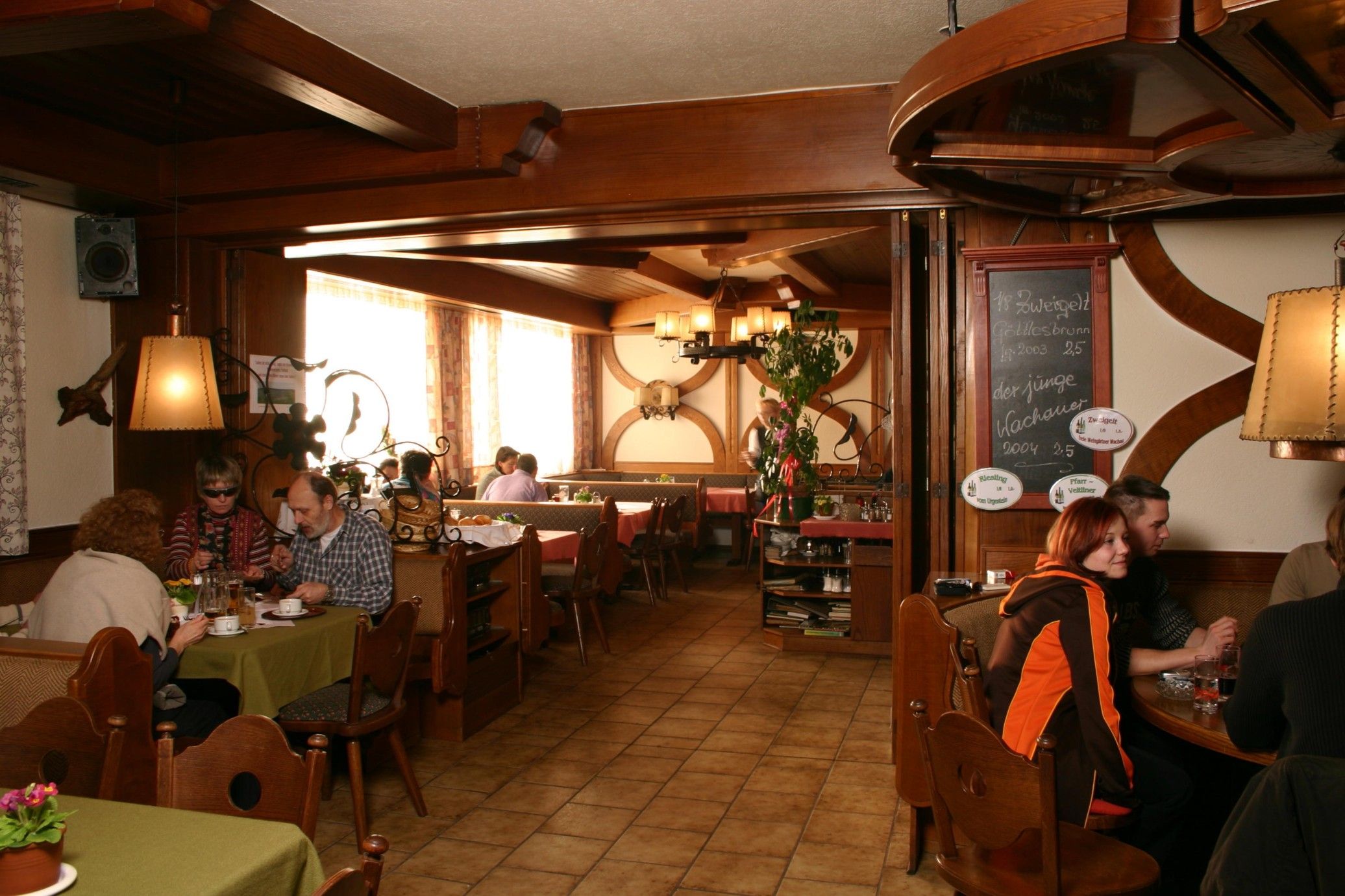 Útulná restaurace s dřevěným nábytkem a hosty u stolů.