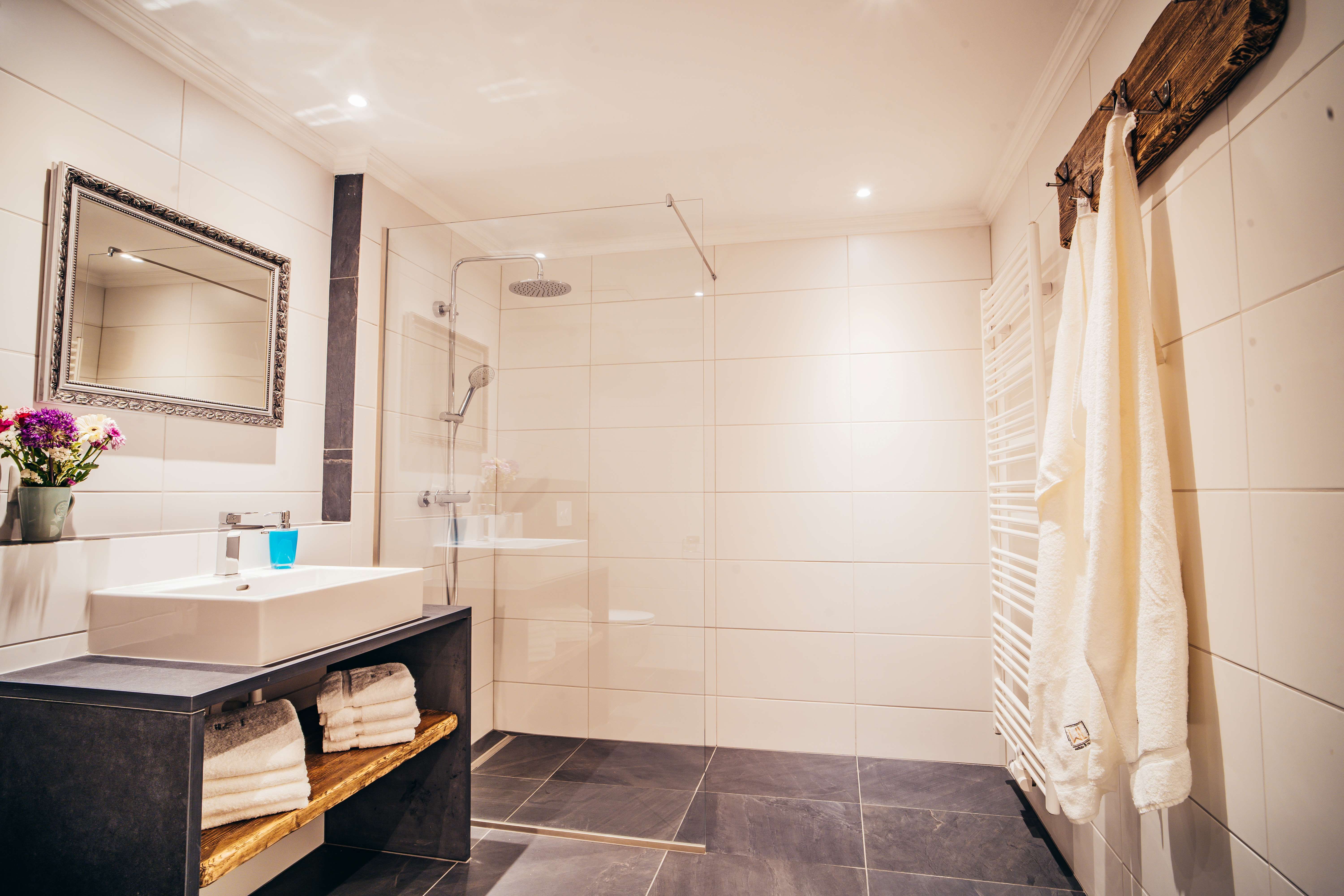 Moderní koupelna s velkým sprchovým koutem, umyvadlem, zrcadlem a ručníky.