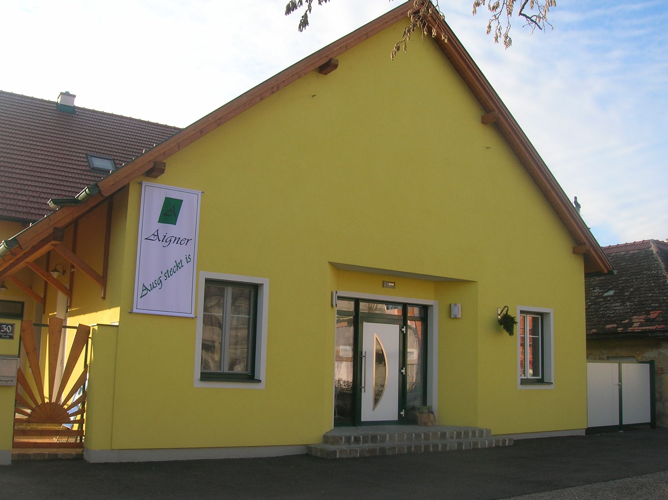Žlutá budova s nápisem "Aigner Ausg'steckt is" na fasádě.