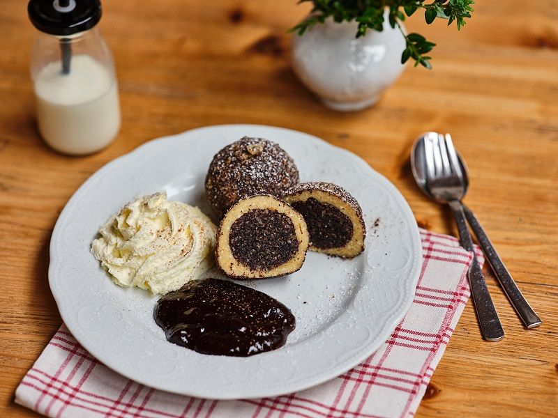 Na dřevěný stůl položte talíř s makovými knedlíky, smetanou a čokoládovou omáčkou.