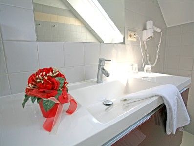 Moderní koupelna s umyvadlem, ručníkem, fénem a květinovou výzdobou.