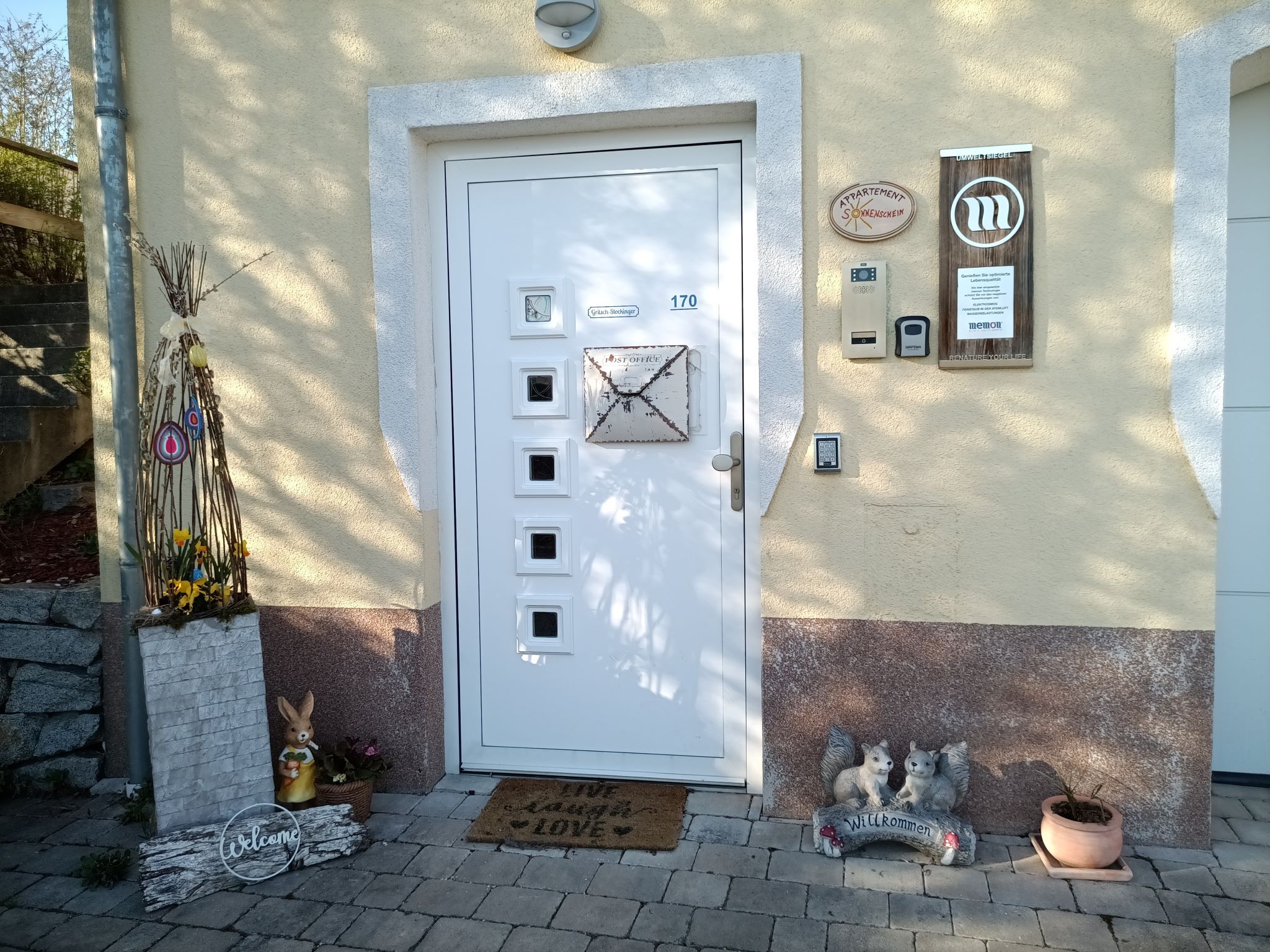 Vstupní prostor domu s dekorativními prvky, jako je králík, uvítací cedule a květiny.