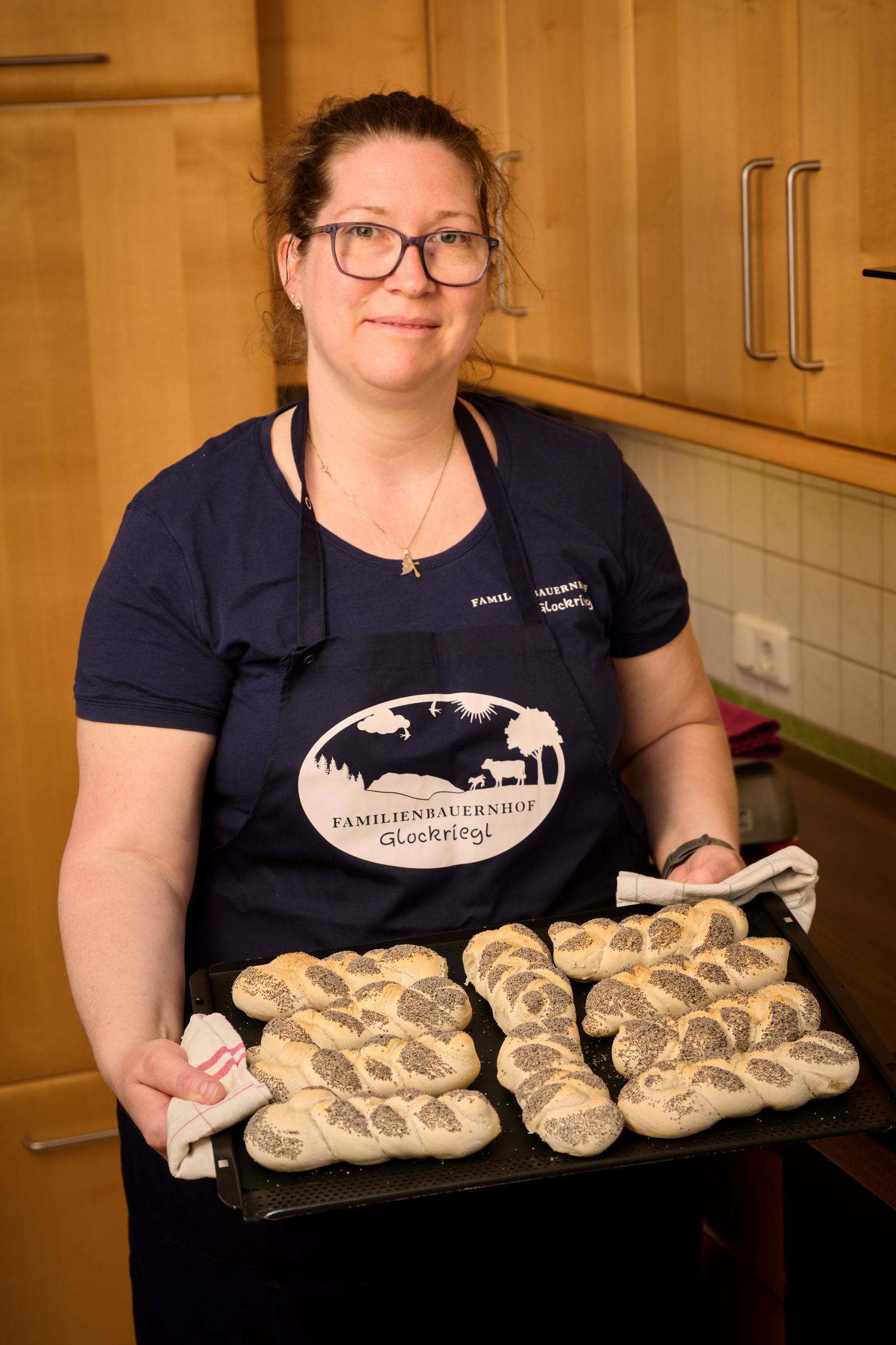Žena v kuchyni drží tác s čerstvě upečenými makovými rohlíčky.