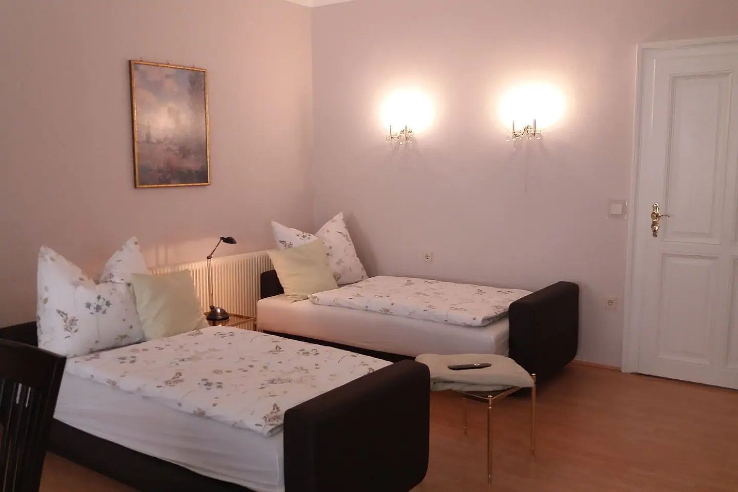 Dvě samostatné postele ve světlém pokoji s nástěnnými lampami a obrazem na stěně.