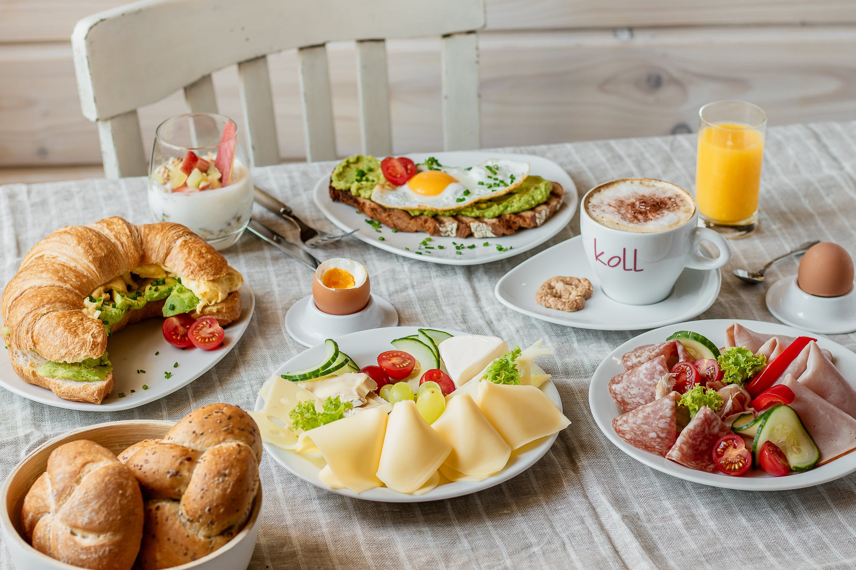 Bohatá snídaně s croissantem, chlebem, sýrem, uzeninami, vejcem, jogurtem, kávou a pomerančovým džusem na stole.