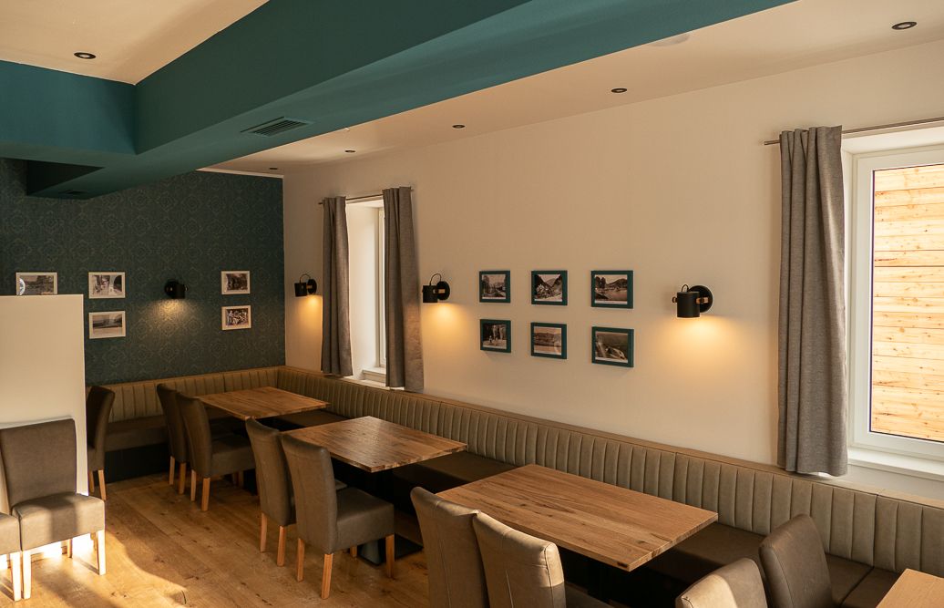 Pohled do interiéru restaurace s dřevěnými stoly, čalouněnými lavicemi a židlemi, zdobené obrazy na stěnách.