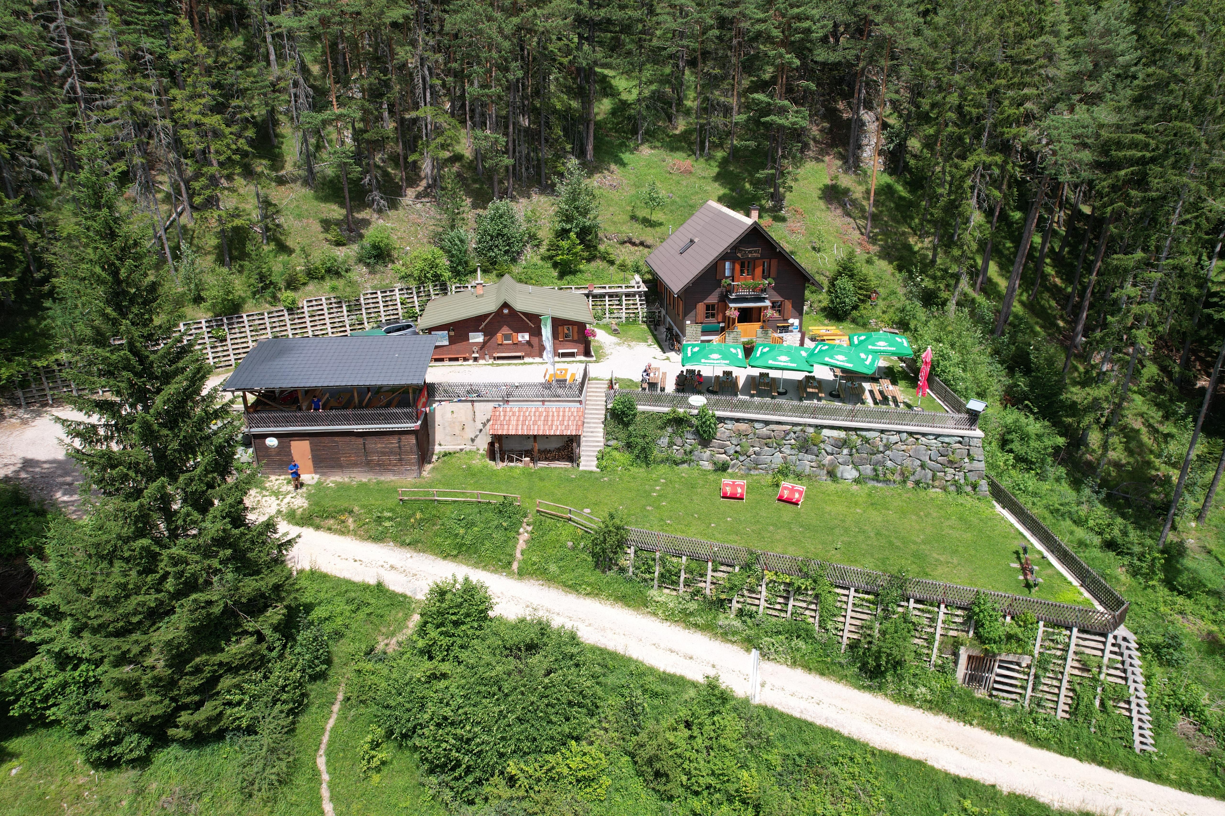 Letecký pohled na chatu Potschacherhütte v zalesněné oblasti s okolními stromy a terasou se slunečníky.