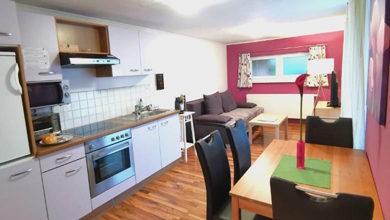 Pohled do interiéru moderního bytu s kuchyní, jídelním stolem a pohovkou.