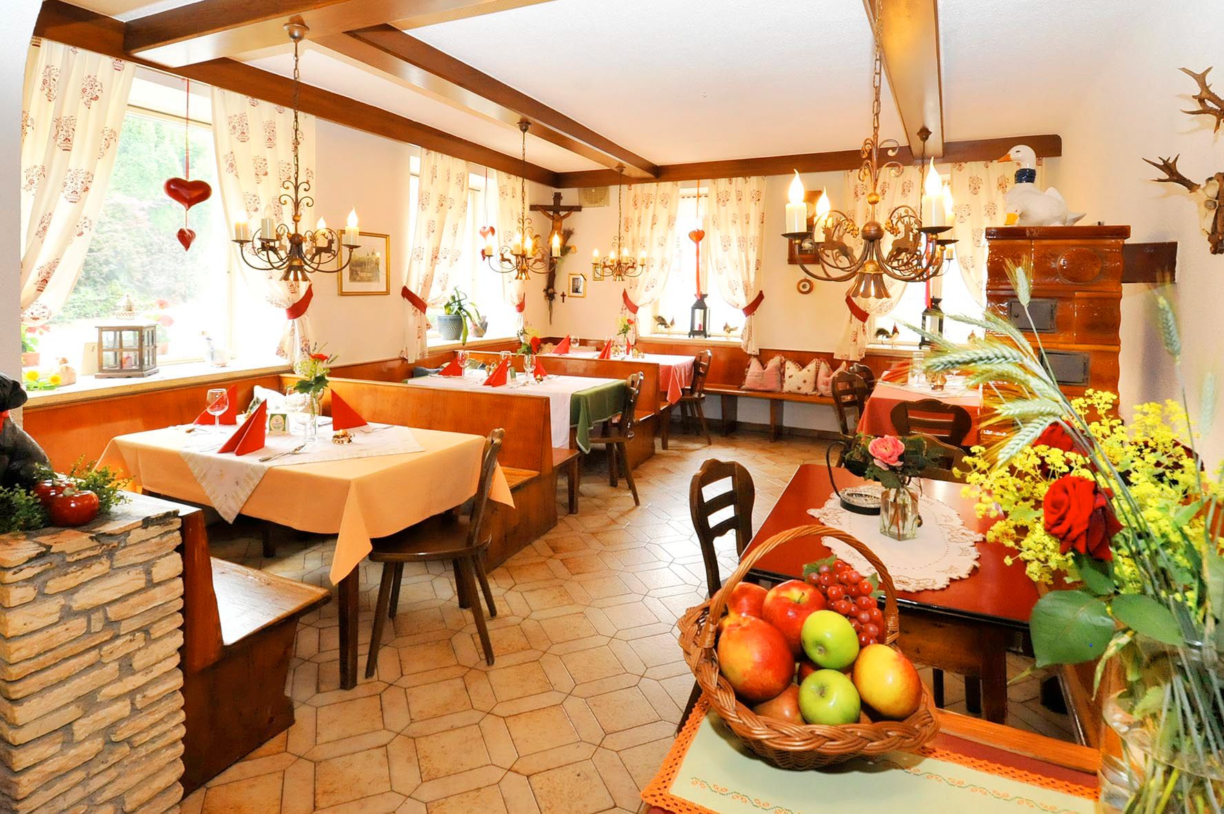 Útulná restaurace s dřevěným nábytkem, dekorativními závěsy a květinovou výzdobou.