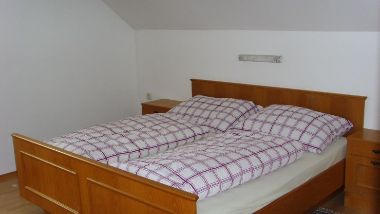 Ložnice s dřevěnou postel&iacute; a kostkovan&yacute;m povlečen&iacute;m.