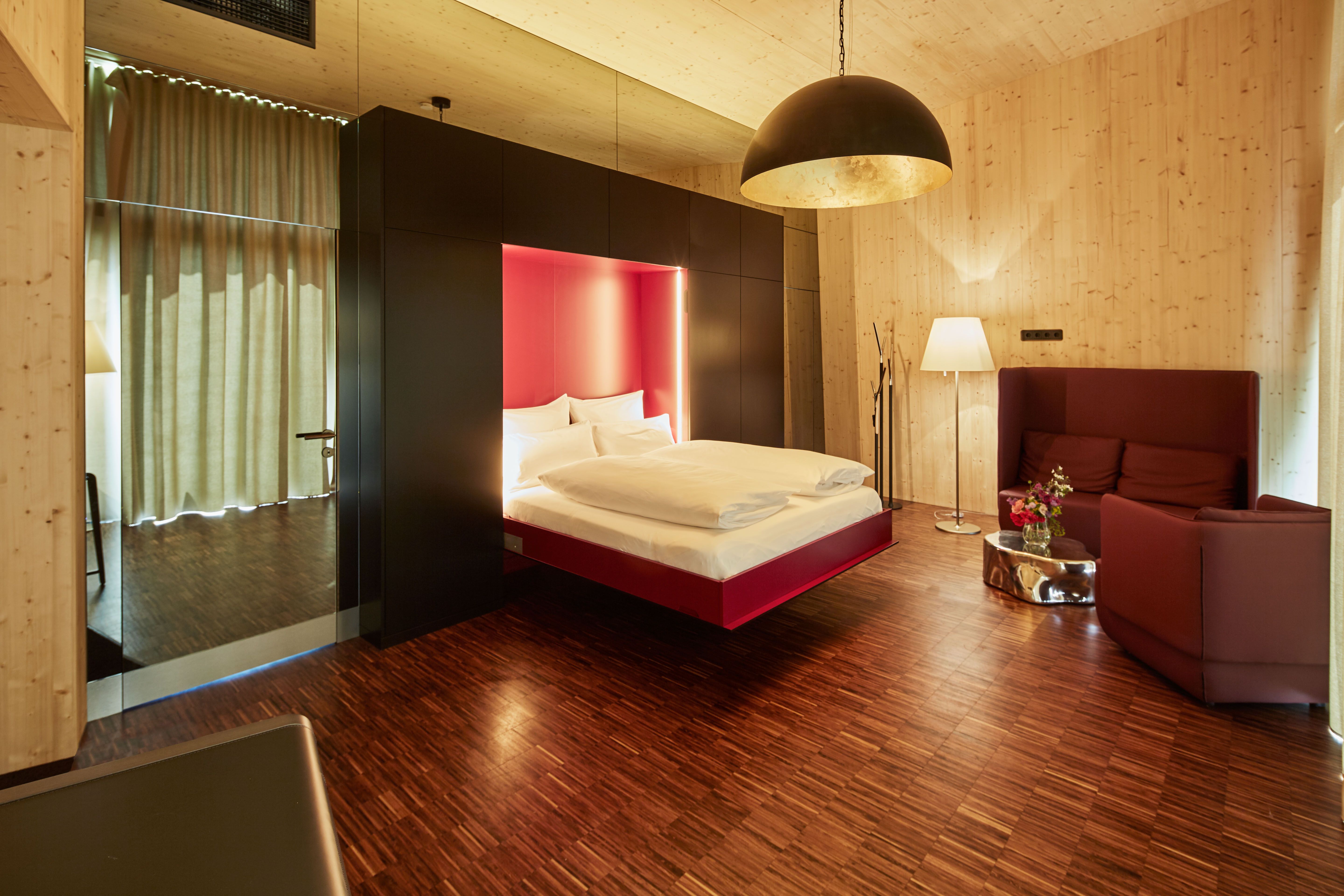 Pohled do interiéru moderní ložnice s plovoucí postelí, dřevěným obložením a stylovým osvětlením.