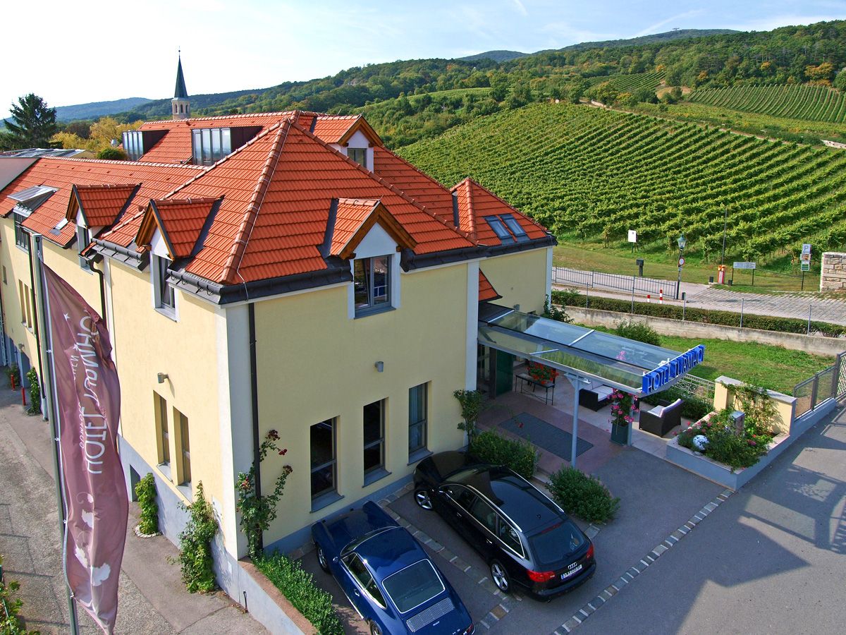 Pohled zvenčí na hotel Turmhof s červenými střechami a okolními vinicemi.