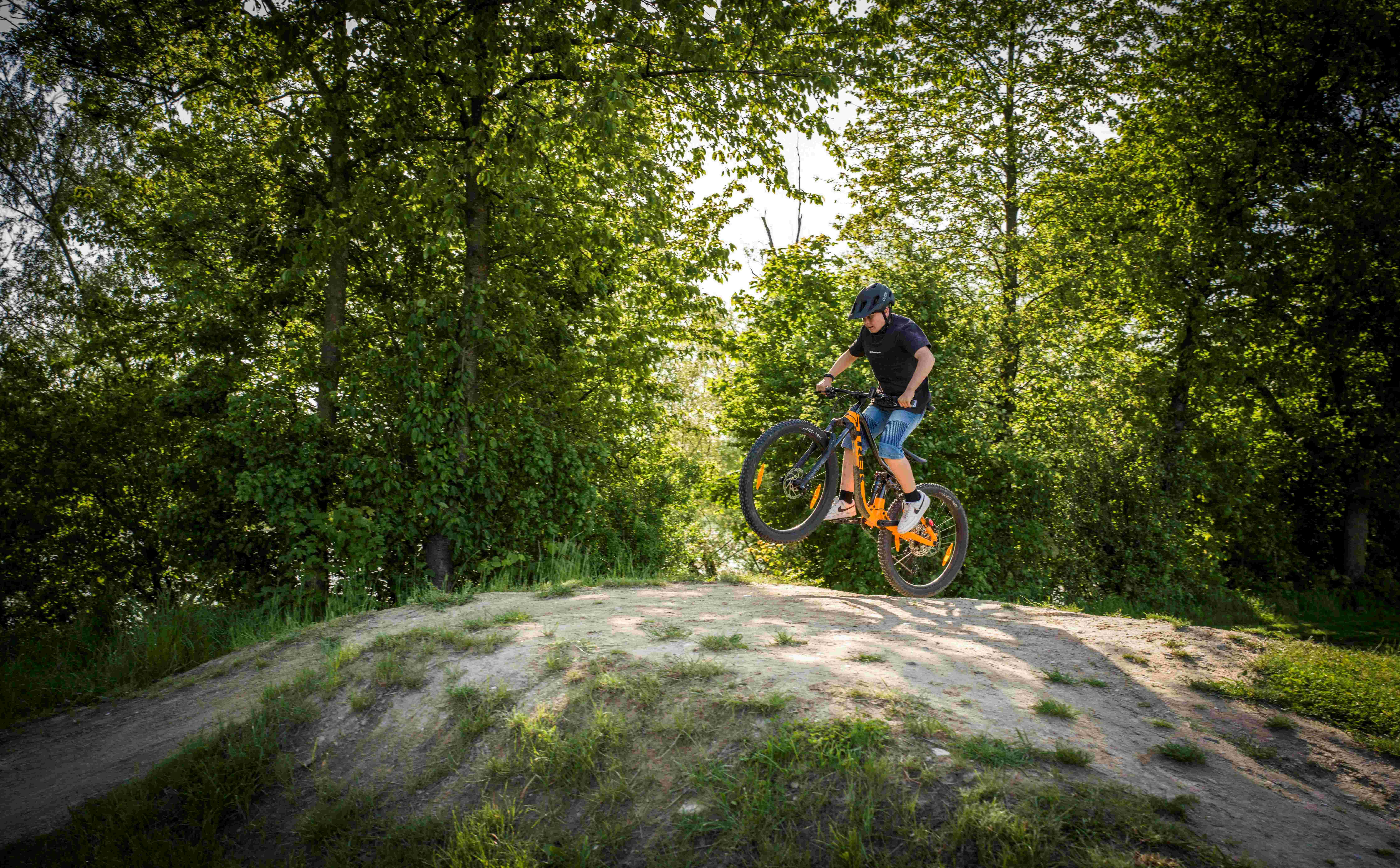Cyklista na horském kole skáče na kole přes kopec v zalesněné oblasti.