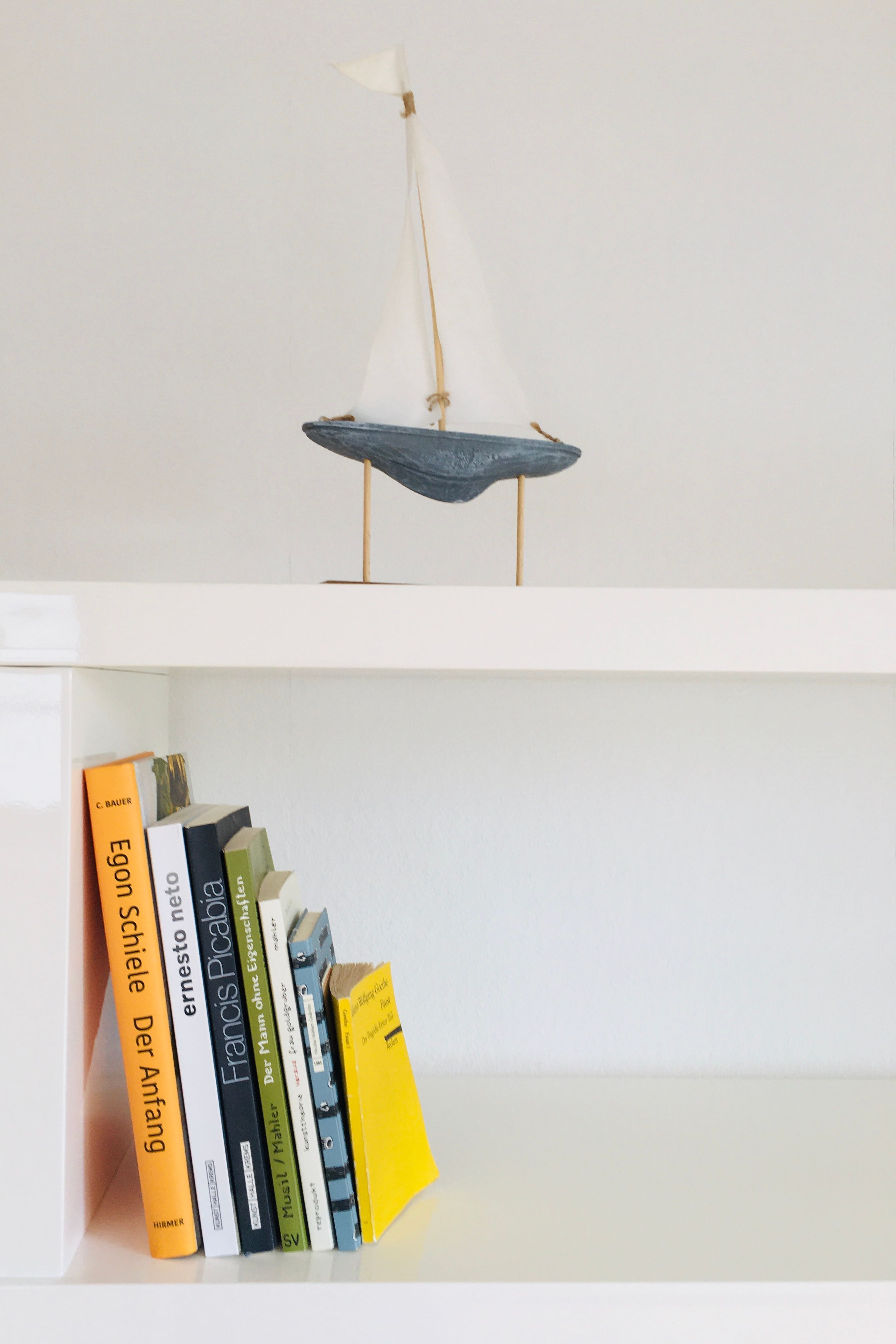 Bílá police s knihami a malou plachetnicí jako dekorací.
