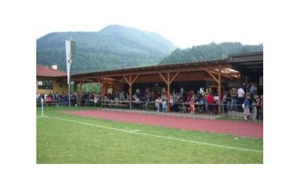 Dav lidí na sportovním hřišti s horami v pozadí.