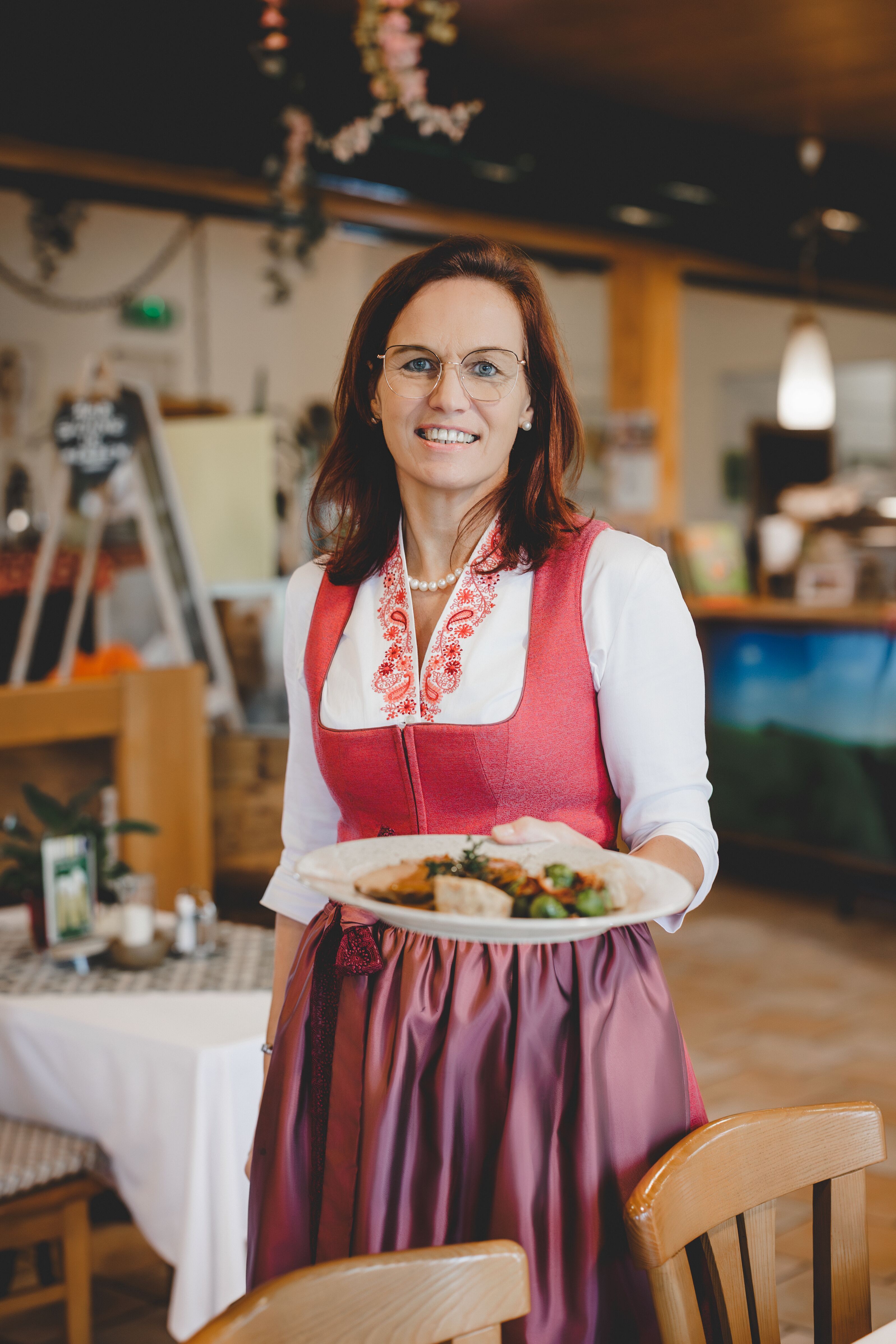 Žena v tradičním kroji podává pokrm v restauraci.