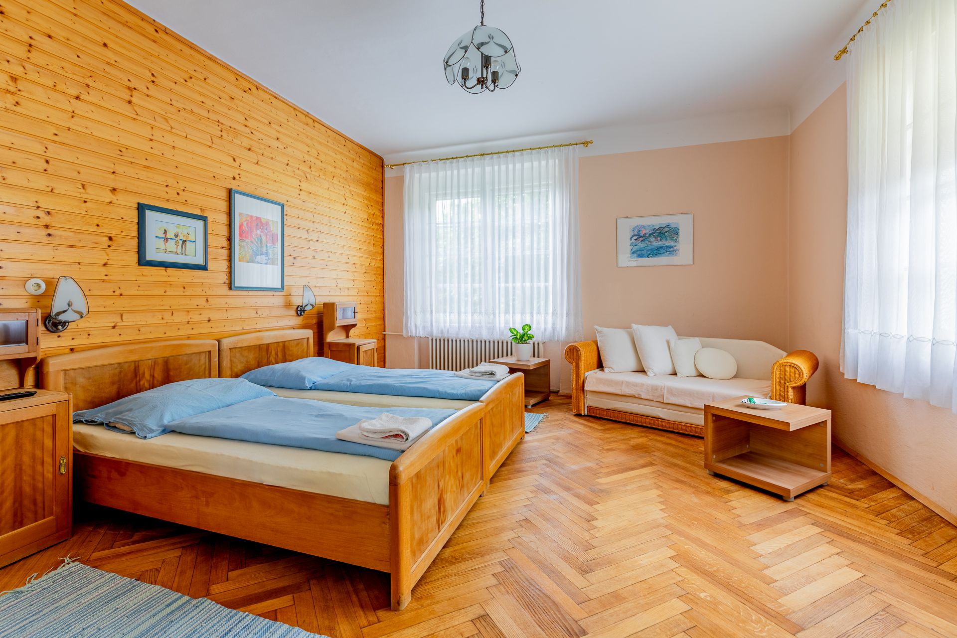 Útulná ložnice s dřevěnými stěnami, dvěma lůžky, pohovkou a dřevěnou podlahou.