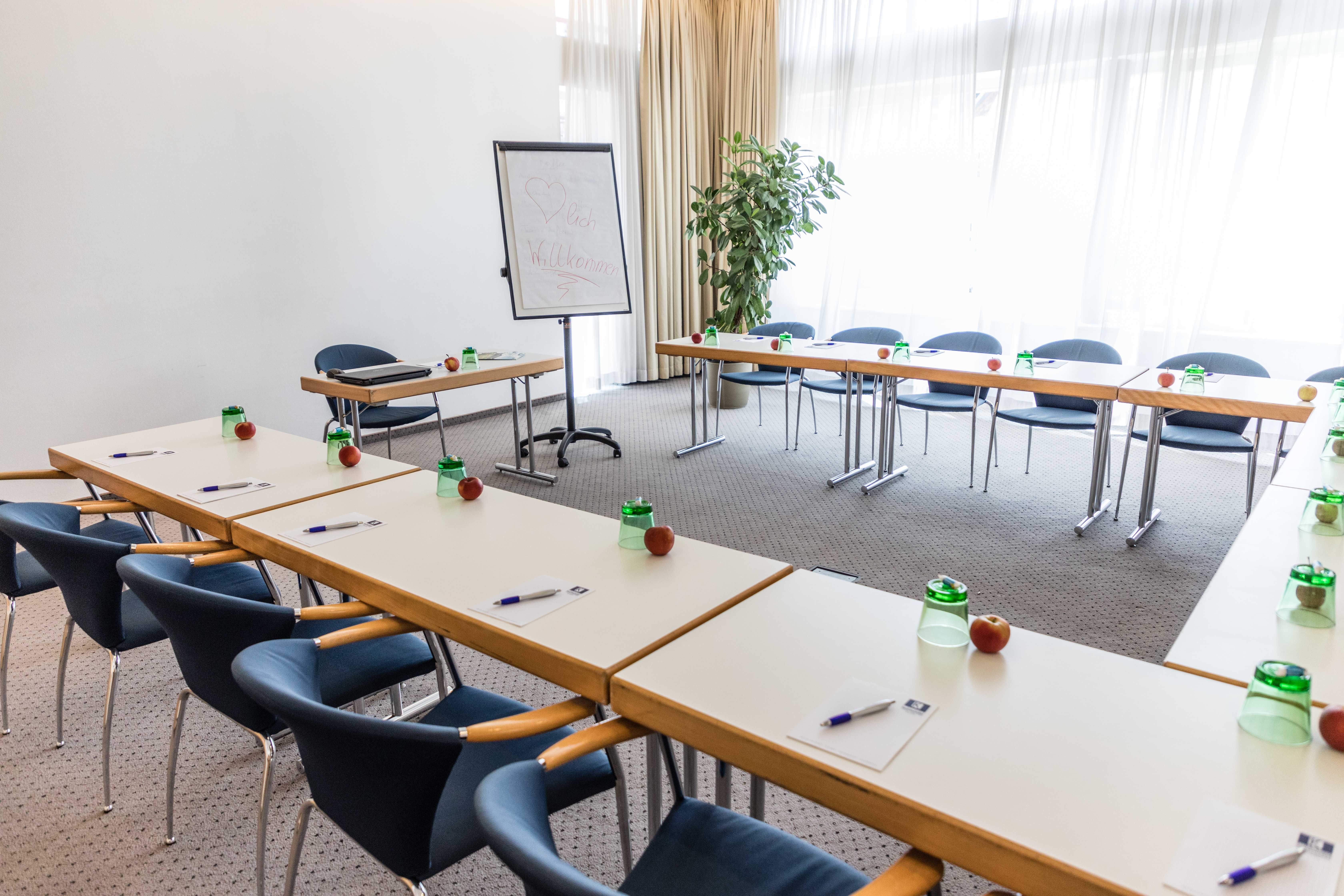 Konferenční místnost se stoly ve tvaru U, židlemi, flipchartem a psacími potřebami.