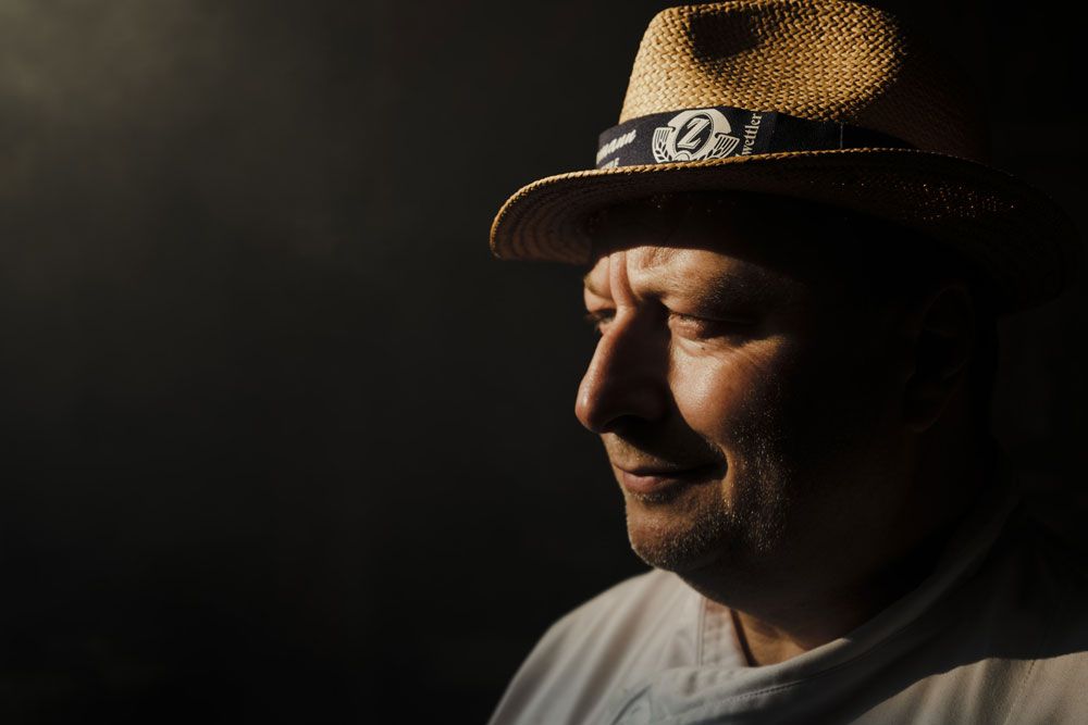 Portrét muže se slaměným kloboukem z profilu, stojícího ve stínu.