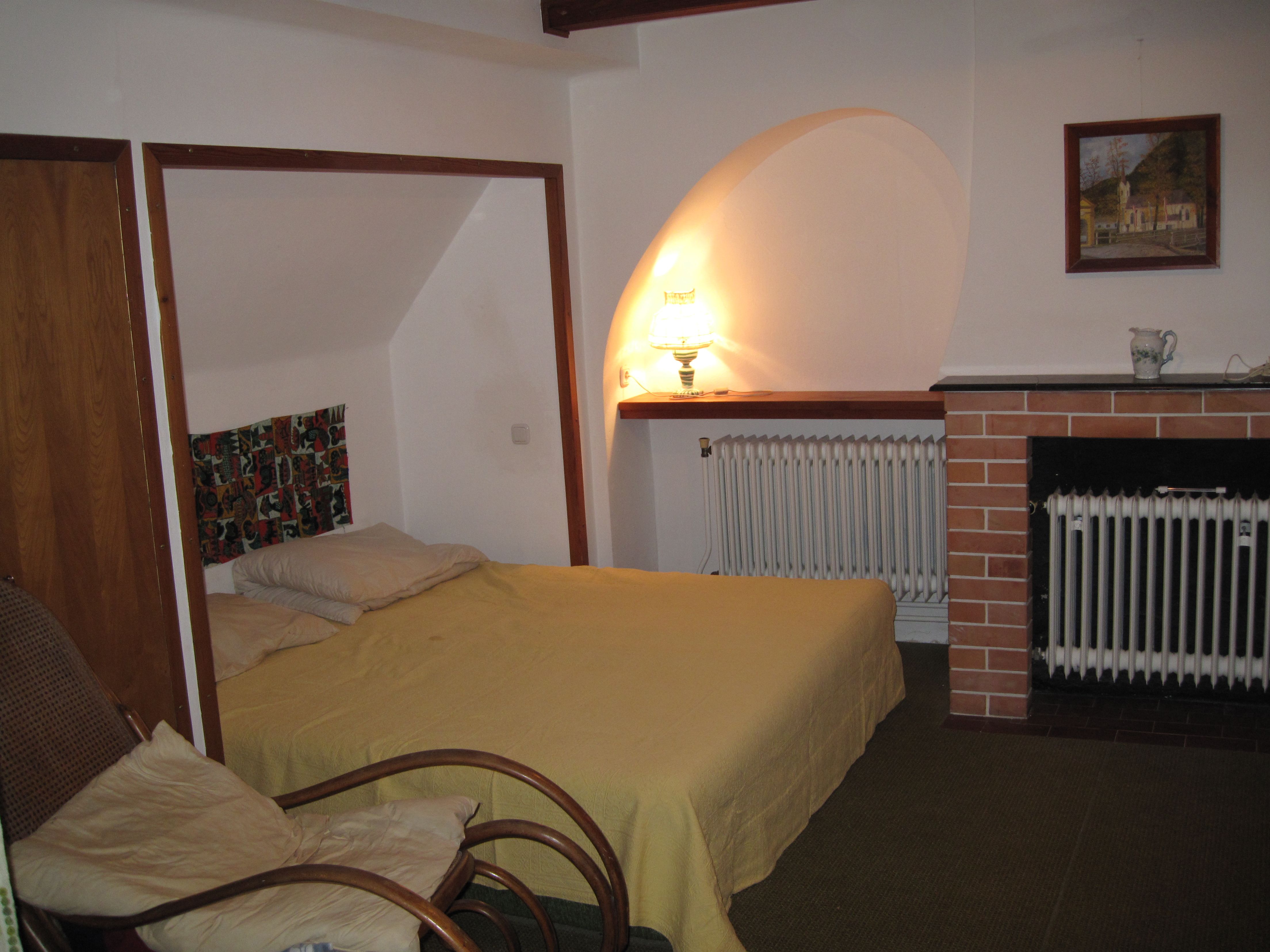 Útulná ložnice s postelí, křeslem, lampou a krbem.