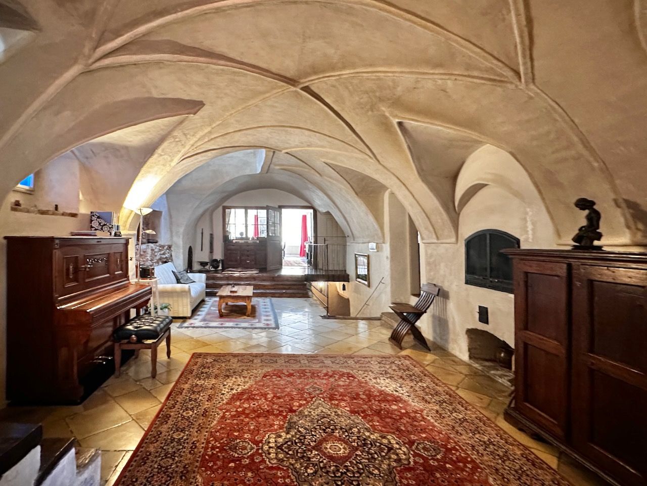 Historická přijímací hala s klenutým stropem, kobercem, klavírem a dřevěným nábytkem.