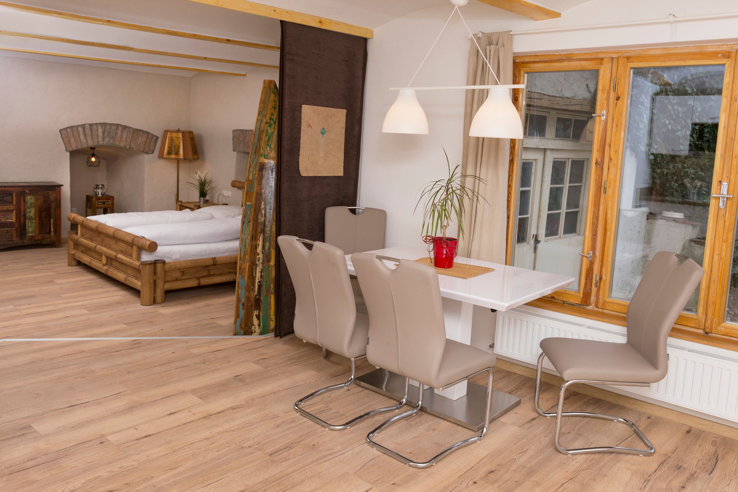 Pohled do interiéru rekreačního bytu s jídelním stolem, židlemi, postelí a oknem.