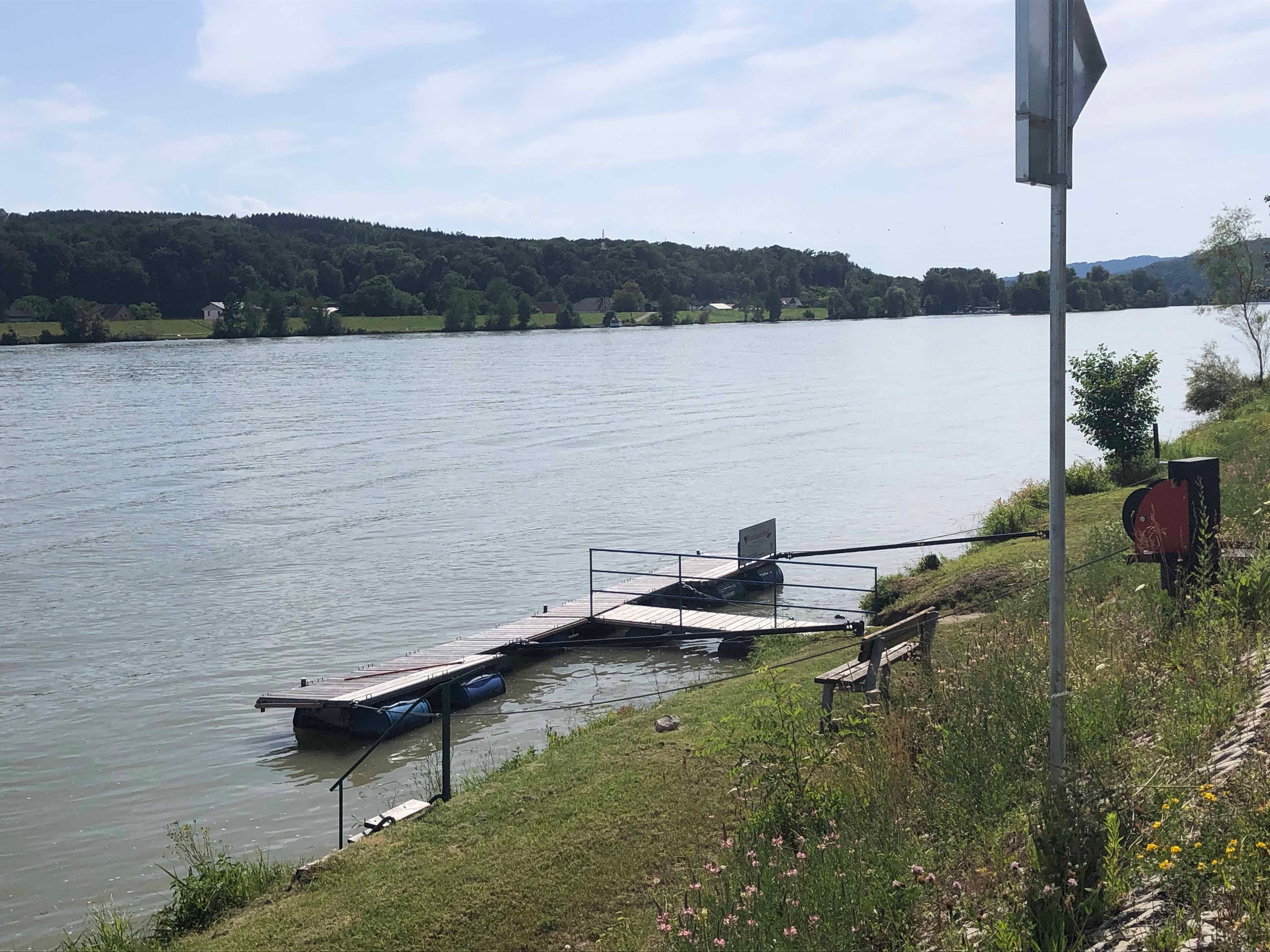 Molo na břehu řeky s lavičkou a vegetací.