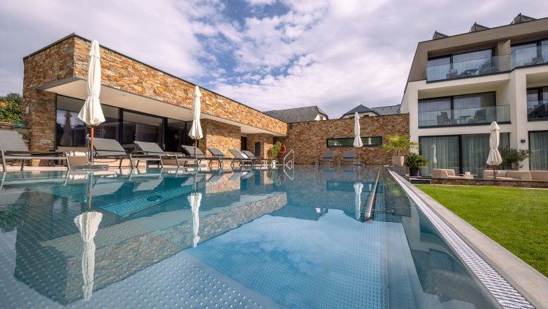 Pohled zvenčí na moderní hotel s bazénem a lehátky.