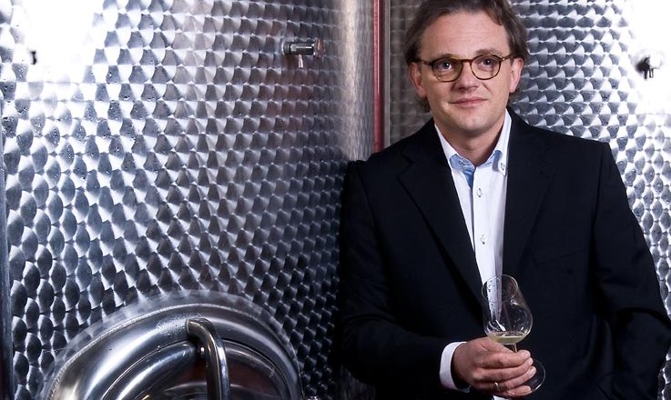 Muž v obleku drž&iacute; sklenici s v&iacute;nem před velkou nerezovou n&aacute;drž&iacute;.