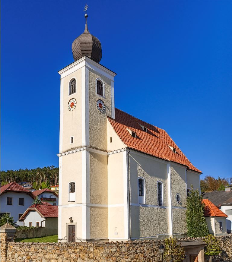 Hollenthonský farní kostel s cibulovou kopulí a modrou oblohou.