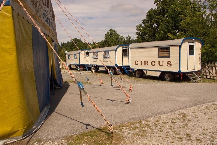 Cirkusový vůz a stan na štěrkovém prostranství.