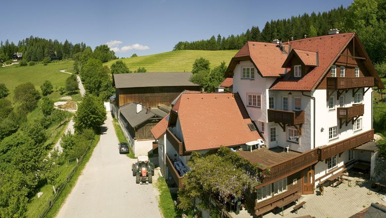 Statek s červenými střechami ve venkovském prostředí, obklopený zelenými loukami a lesy.