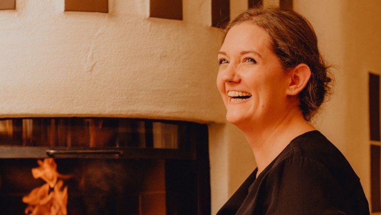 Žena se usmívá před krbem s hořícím ohněm.