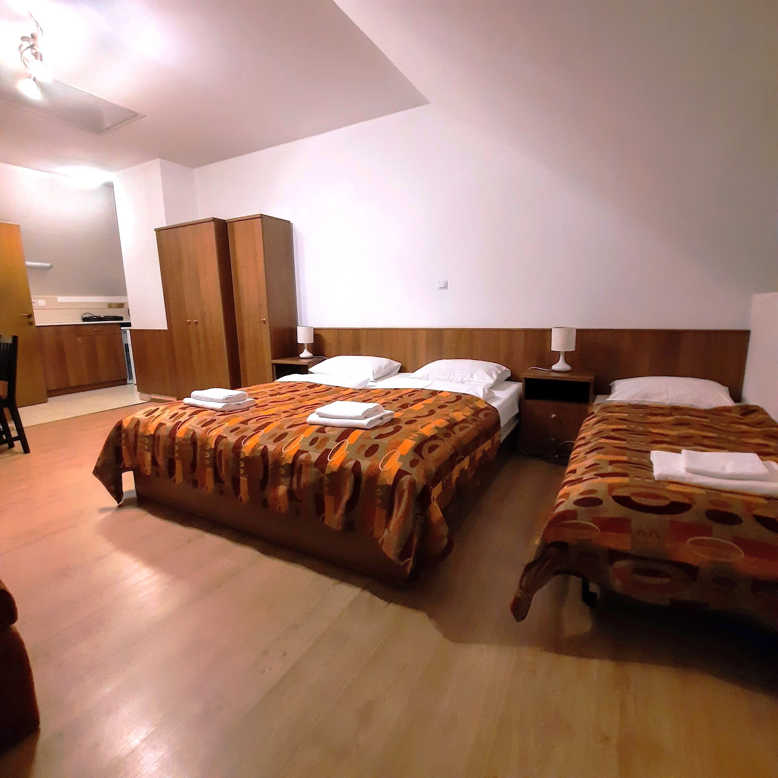 Třílůžkový pokoj se dvěma samostatnými lůžky a manželskou postelí se vzorovanými přikrývkami. K dispozici je také šatní skříň a noční stolky.