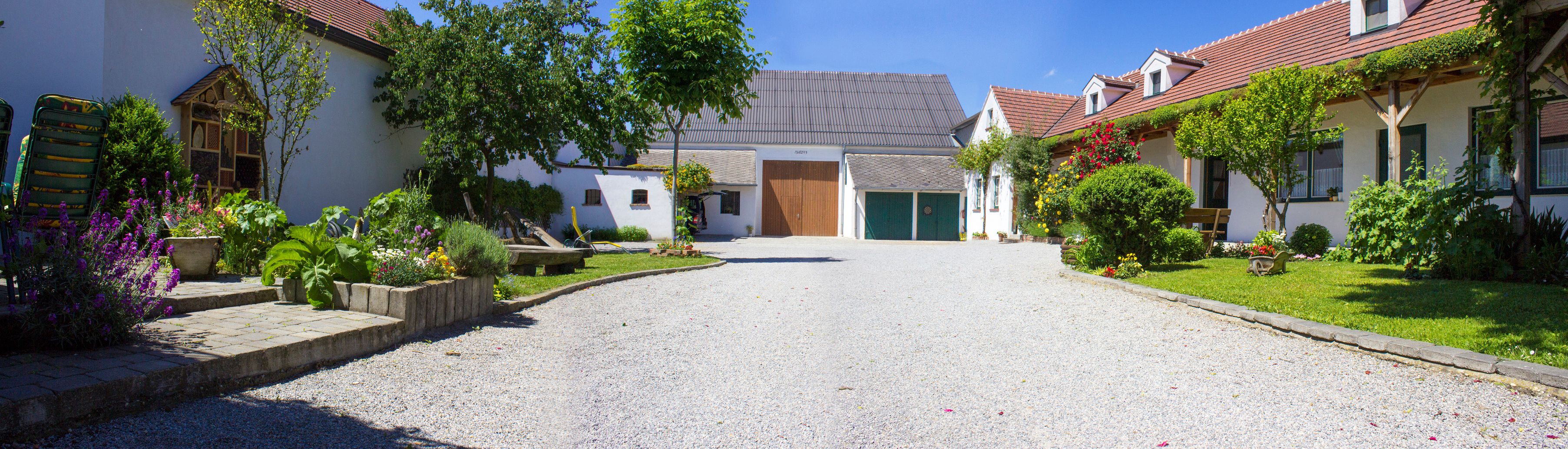 Idylická vinice se štěrkovou cestou, kvetoucími zahradami a tradičními stavbami pod modrou oblohou.