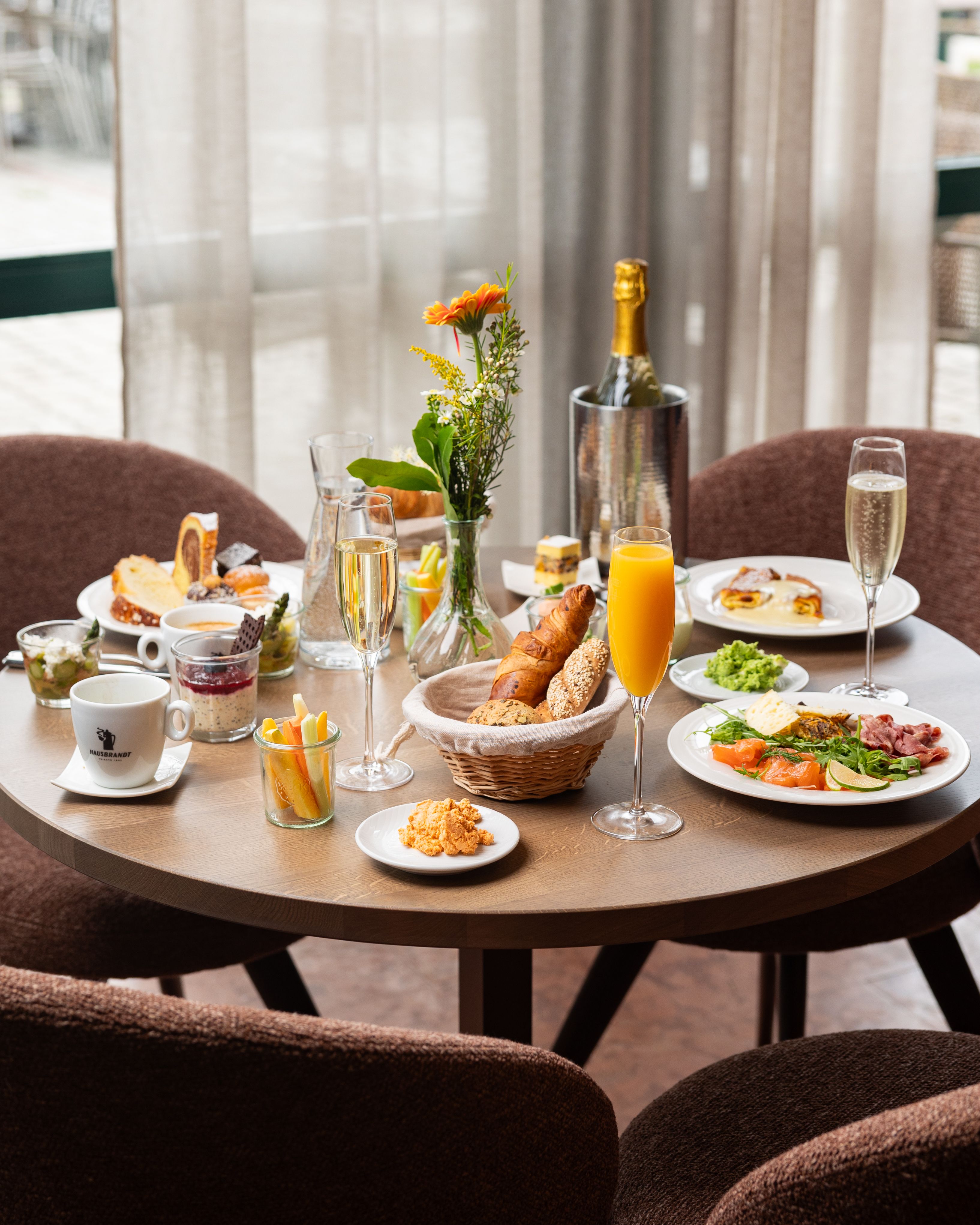 Prostřený snídaňový stůl s různým nádobím, nápoji a květinami.