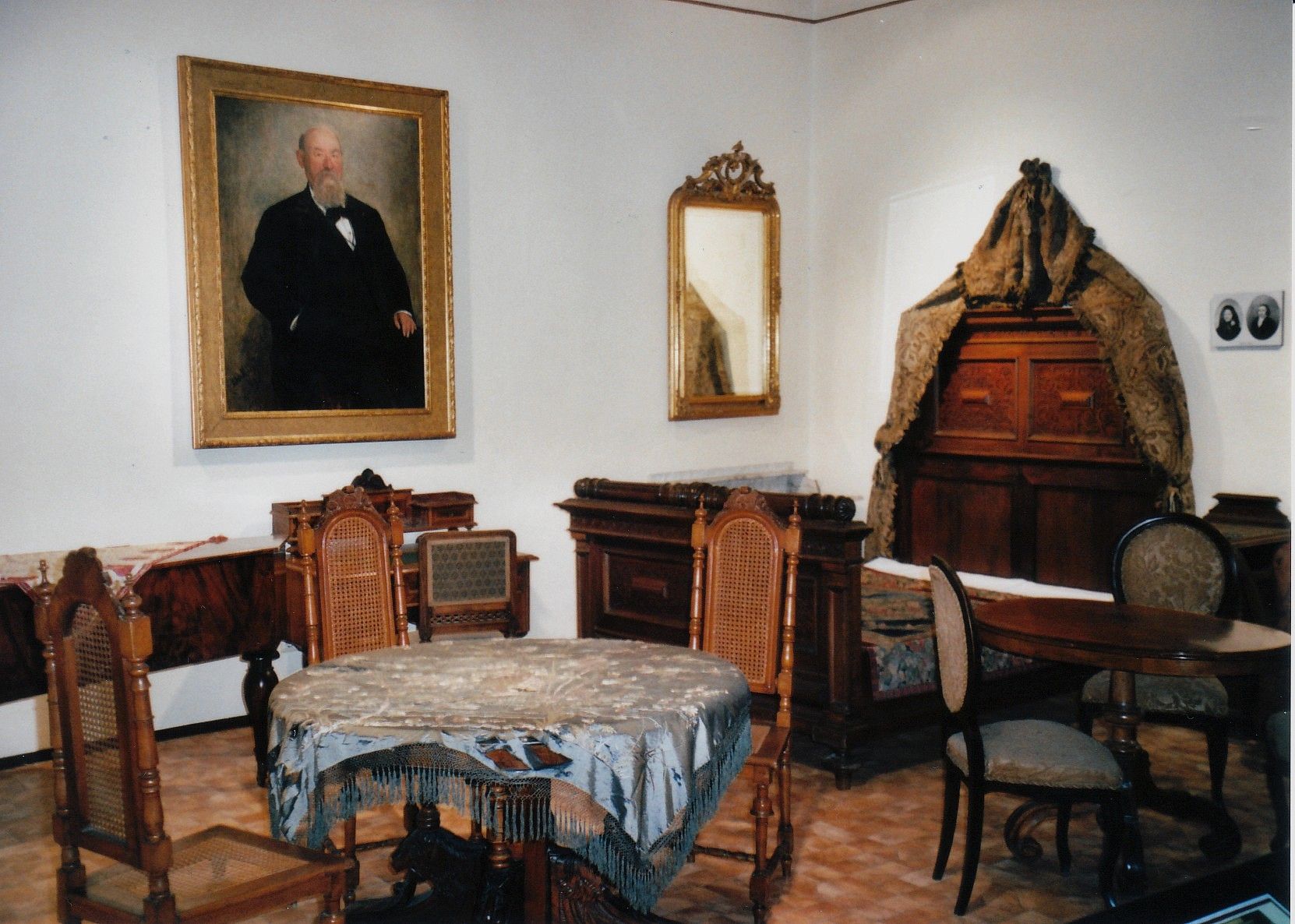 Historický pokoj se starožitným nábytkem a obrazem muže na stěně.