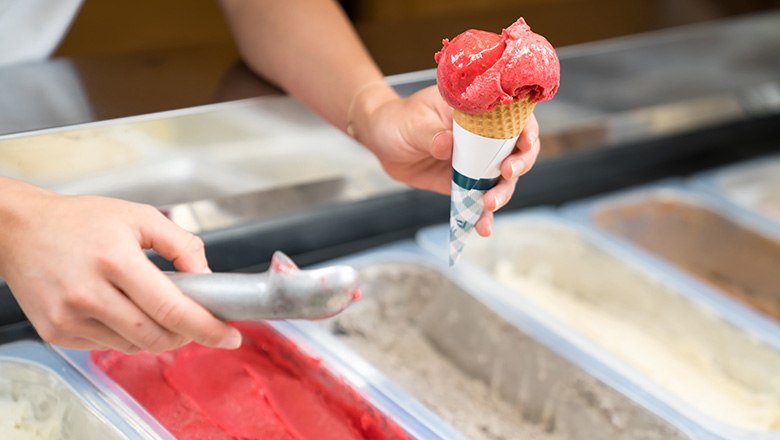 One hand holds an ice cream cone with a scoop of fruit ice cream, the other holds an ice cream scoop., &copy; Blochberger Eisproduktion GmbH