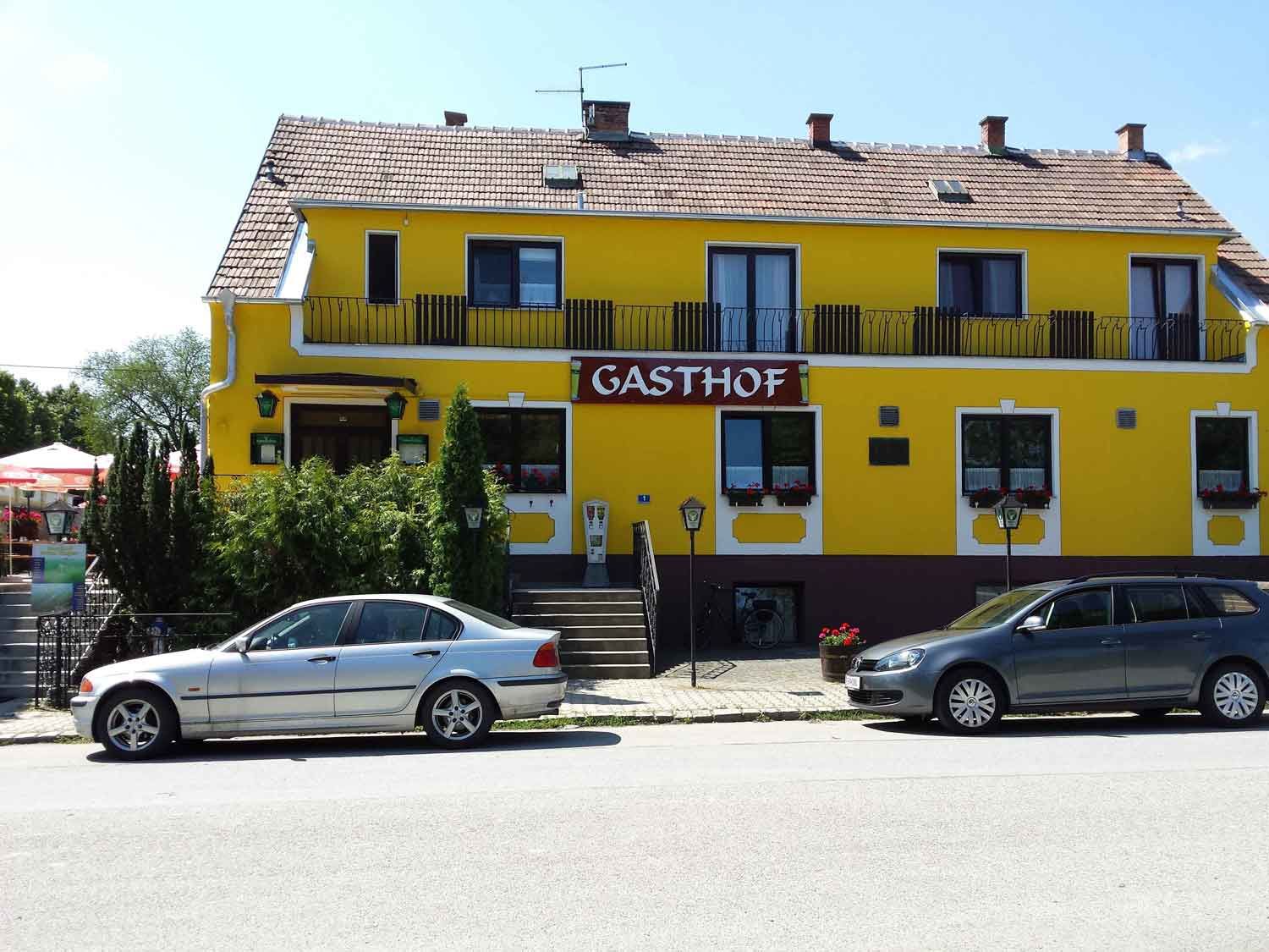 Žlutá budova s nápisem "Gasthof", před ní zaparkovaná auta.