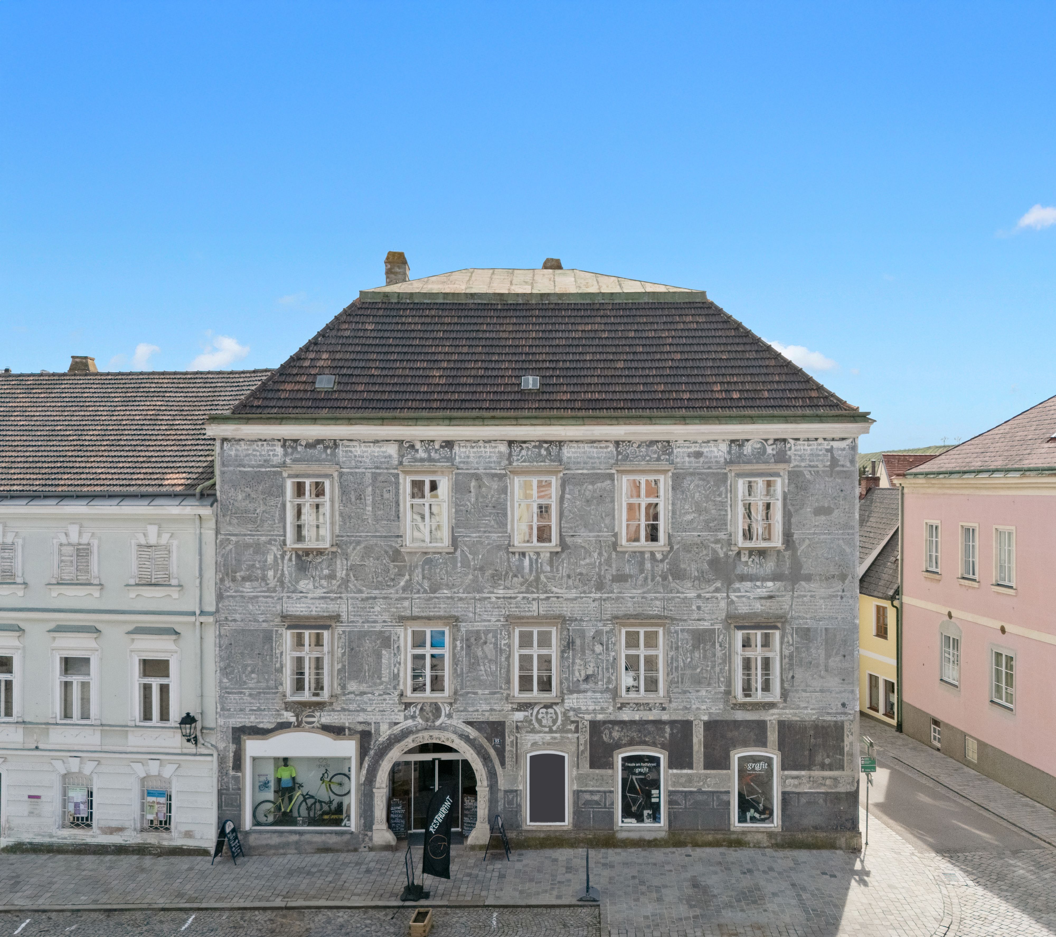 Historická budova s šedou fasádou a dekorativními malbami ve městě.