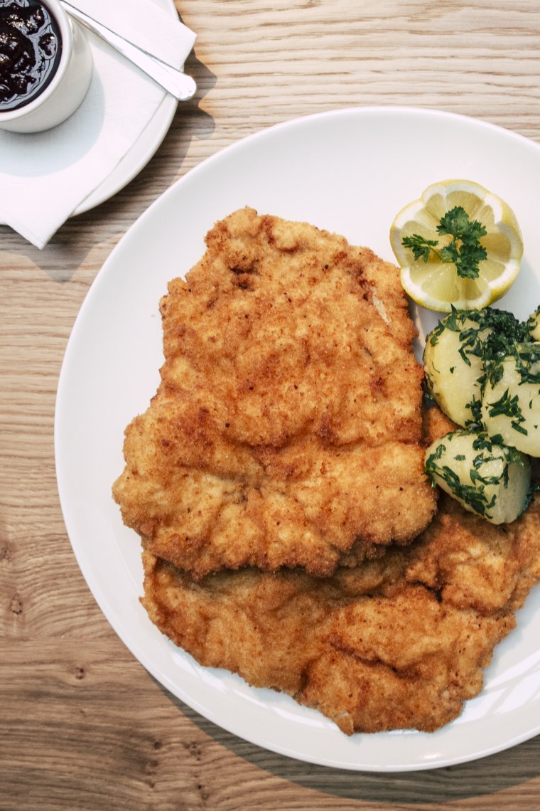Ein Schnitzel, wie es sein soll: perfekt goldbraun gebraten, serviert mit frischen Petersilerdäpfeln und einer fruchtigen Preiselbeersauce., © Astrid Bartl