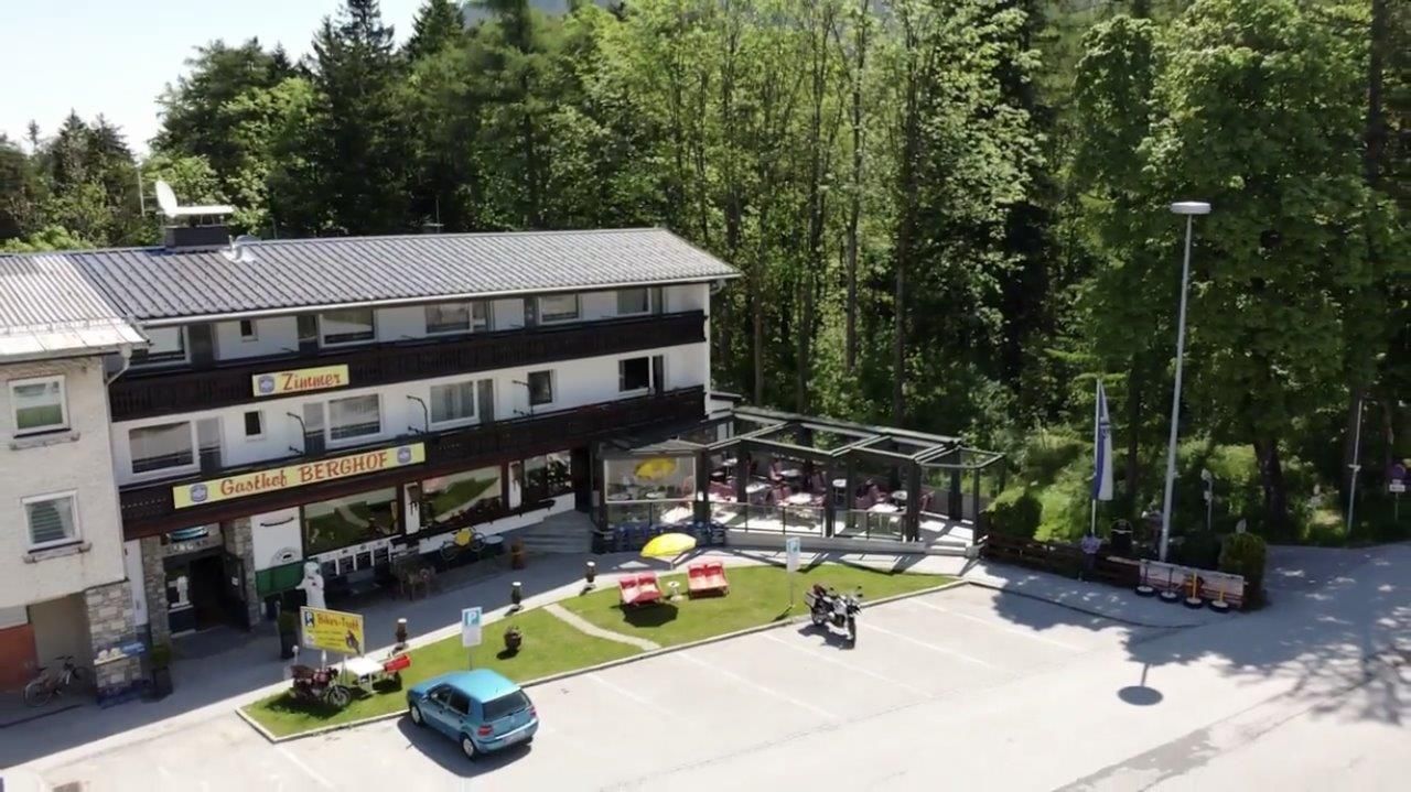 Pohled zvenčí na Gasthof Berghof s terasou a parkovištěm, obklopený stromy.
