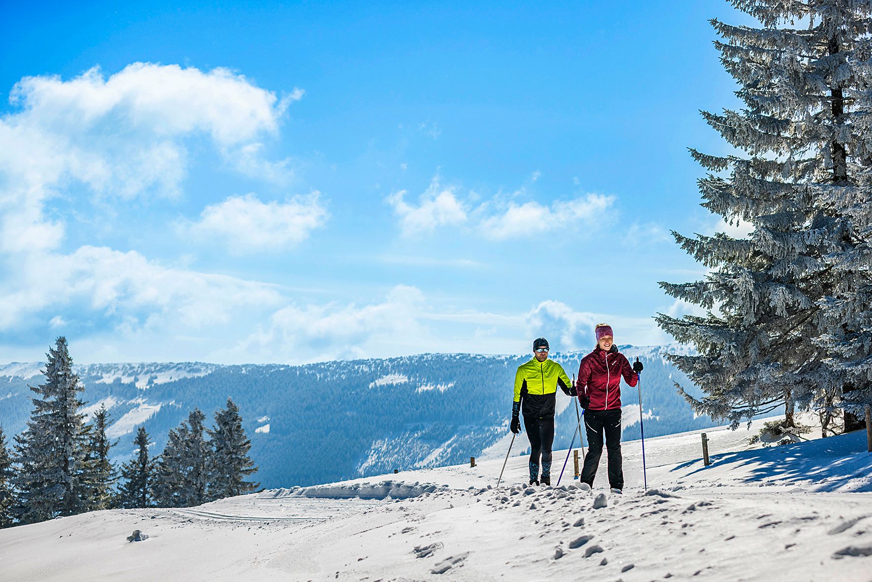 Dva běžkaři na zasněžené trase v zimní horské krajině.