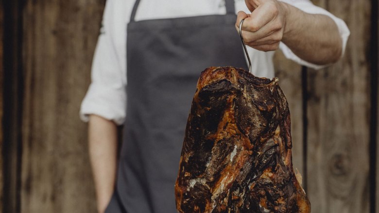 Osoba držící uzenou šunku na háčku.