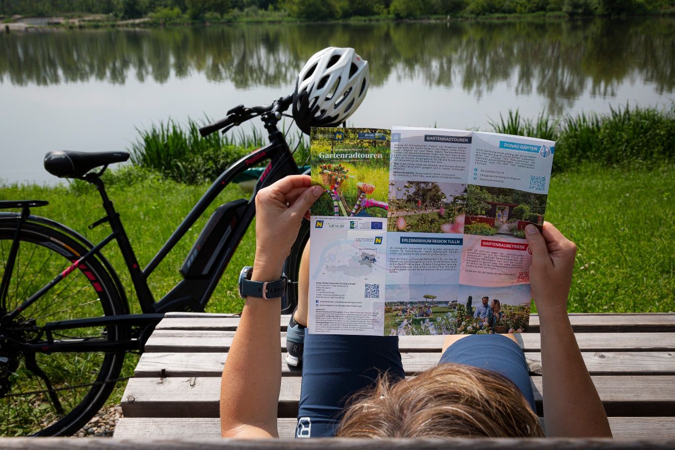 Osoba čte skládací mapu o zahradních cyklistických výletech vedle kola u jezera.