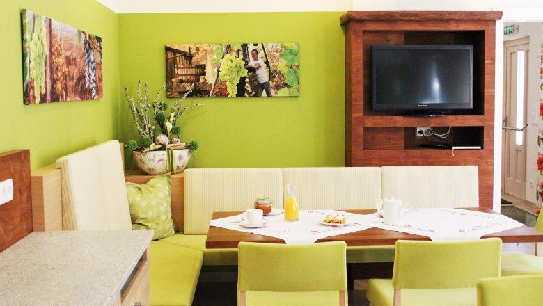 Útulná jídelna se zelenými stěnami, dřevěným nábytkem a TV.